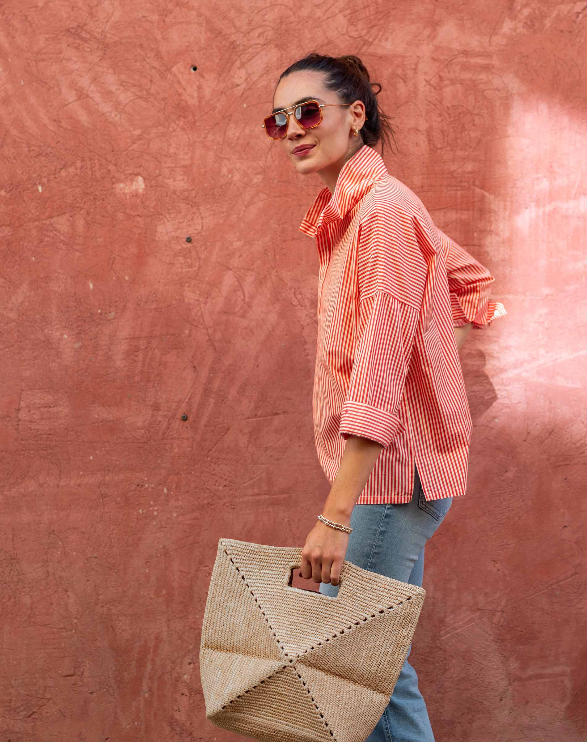 Woman holding a woven bag against a pink wall