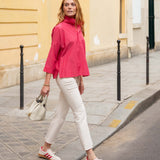 Woman in a pink top and white pants walking on a city street.
