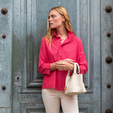 Woman in a pink shirt and white pants standing in front of a textured blue door.