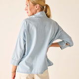 Woman wearing a light blue shirt with rolled-up sleeves on a beige background