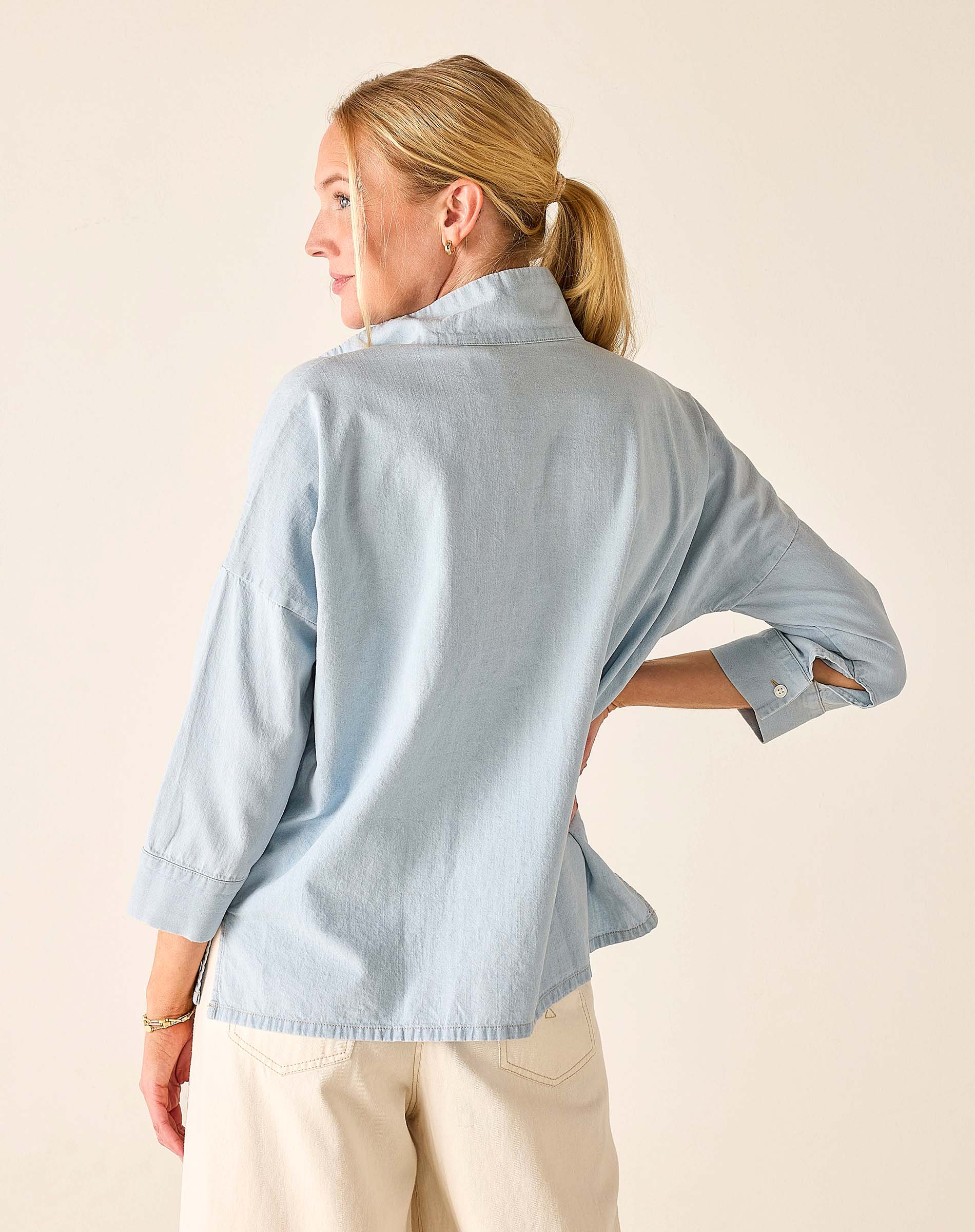 Woman wearing a light blue shirt with rolled-up sleeves on a beige background