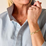 Woman wearing gold jewelry including a necklace and bracelet, with a light blue shirt.