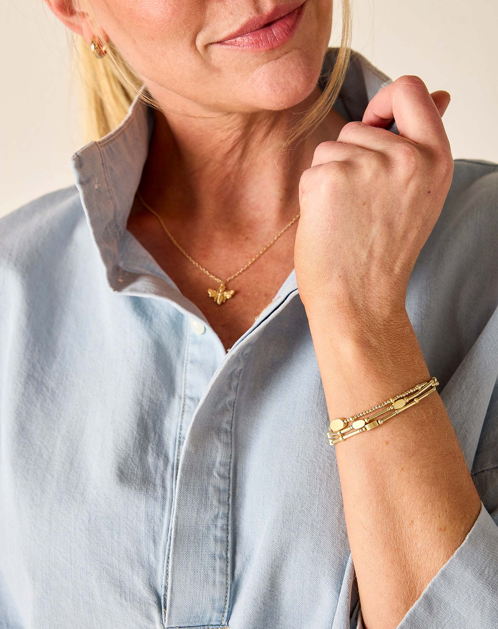 Woman wearing gold jewelry including a necklace and bracelet, with a light blue shirt.