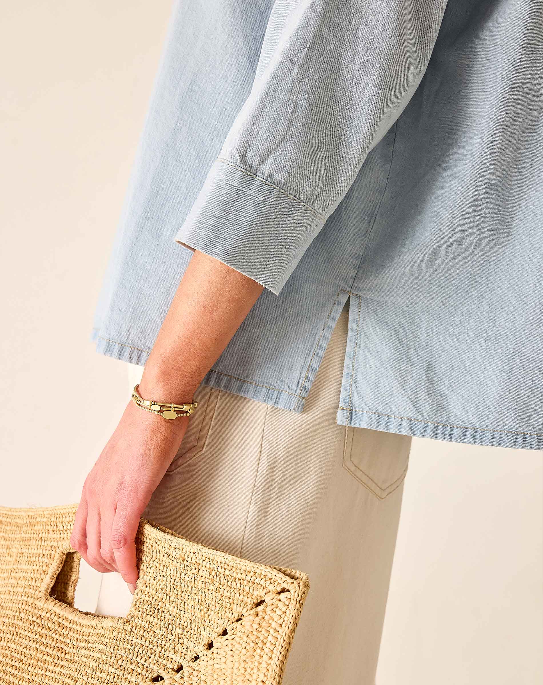 Person wearing a light blue shirt holding a woven bag on a beige background