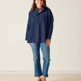Woman wearing a navy blue shirt, jeans, and brown shoes on a plain background