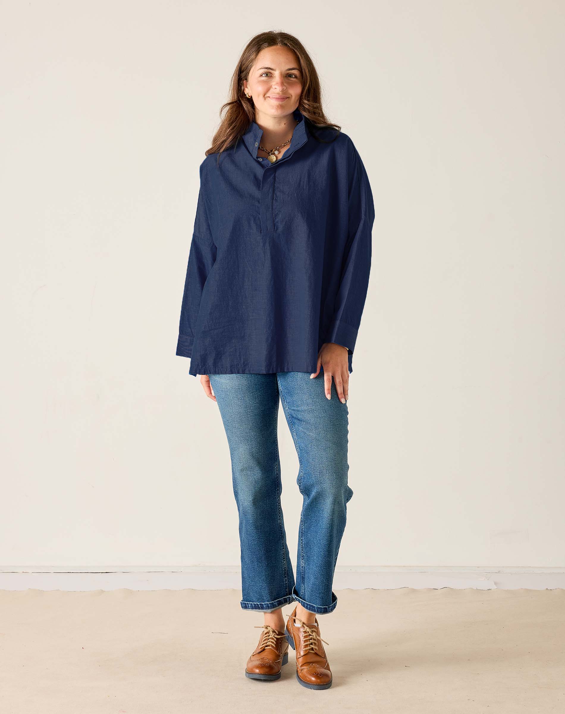 Woman wearing a navy blue shirt, jeans, and brown shoes on a plain background