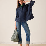 Woman wearing a navy blue shirt and jeans, holding a green bag against a white background