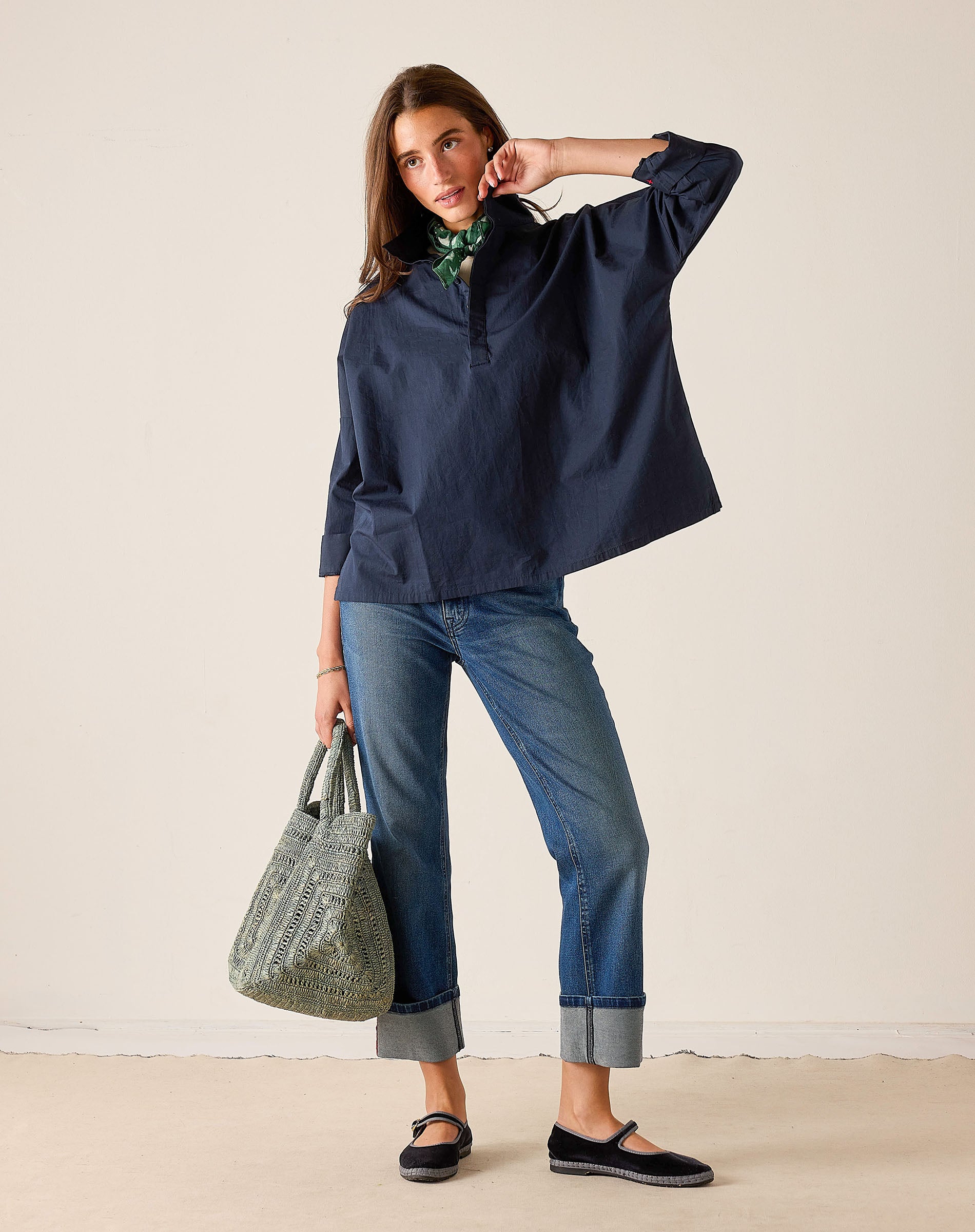 Woman wearing a navy blue shirt and jeans, holding a green bag against a white background