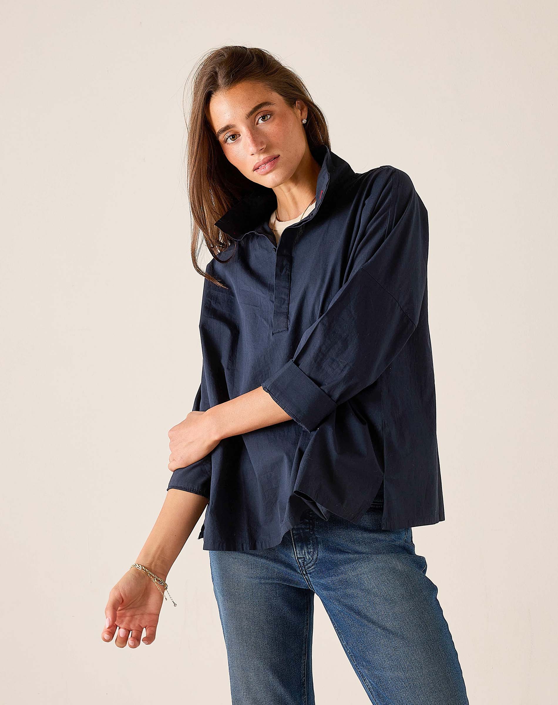 Woman wearing a navy shirt and blue jeans against a plain background