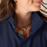 Close-up of a person wearing a gold necklace with a pendant and pearl, against a neutral background.
