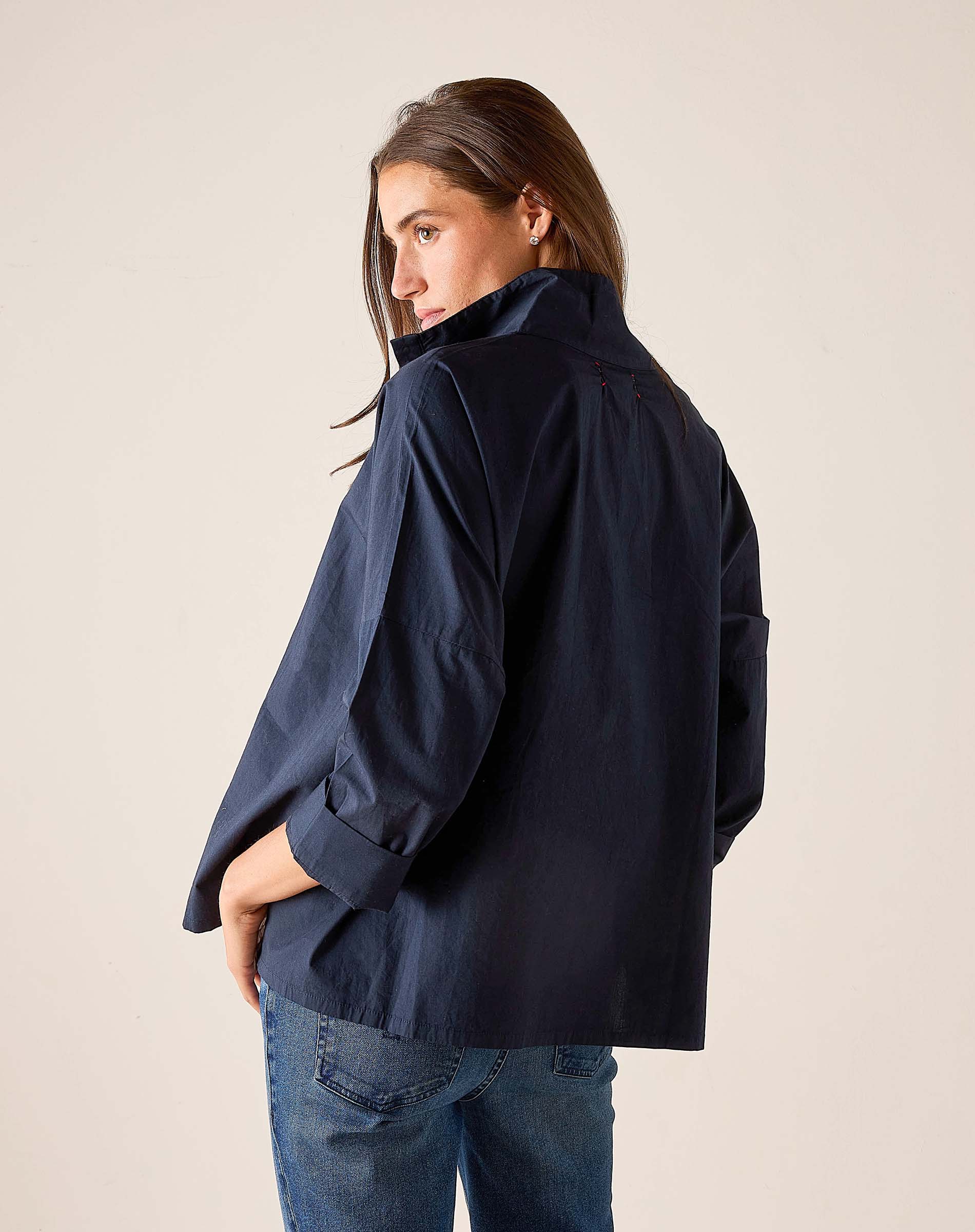 Person wearing a navy jacket and blue jeans against a plain background