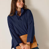 Woman wearing a navy blue shirt holding a brown leather clutch against a plain background