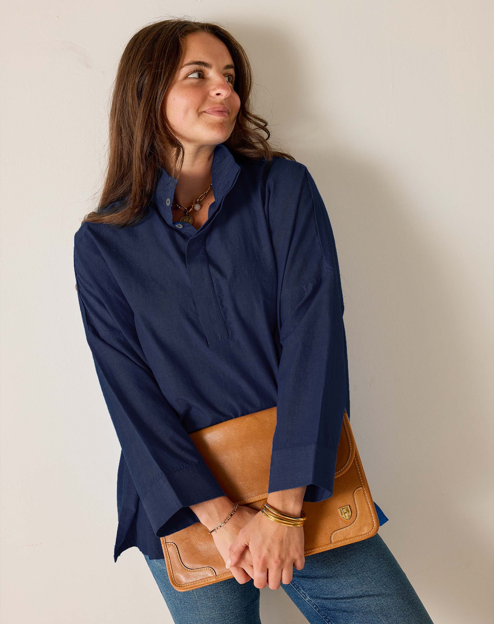 Woman wearing a navy blue shirt holding a brown leather clutch against a plain background