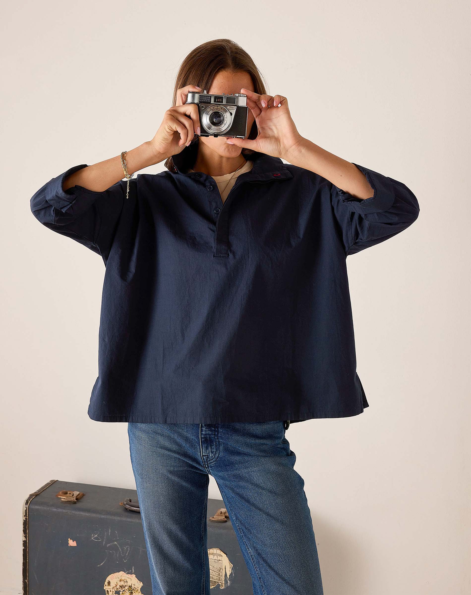 Person wearing a navy blue shirt and blue jeans holding a vintage camera.