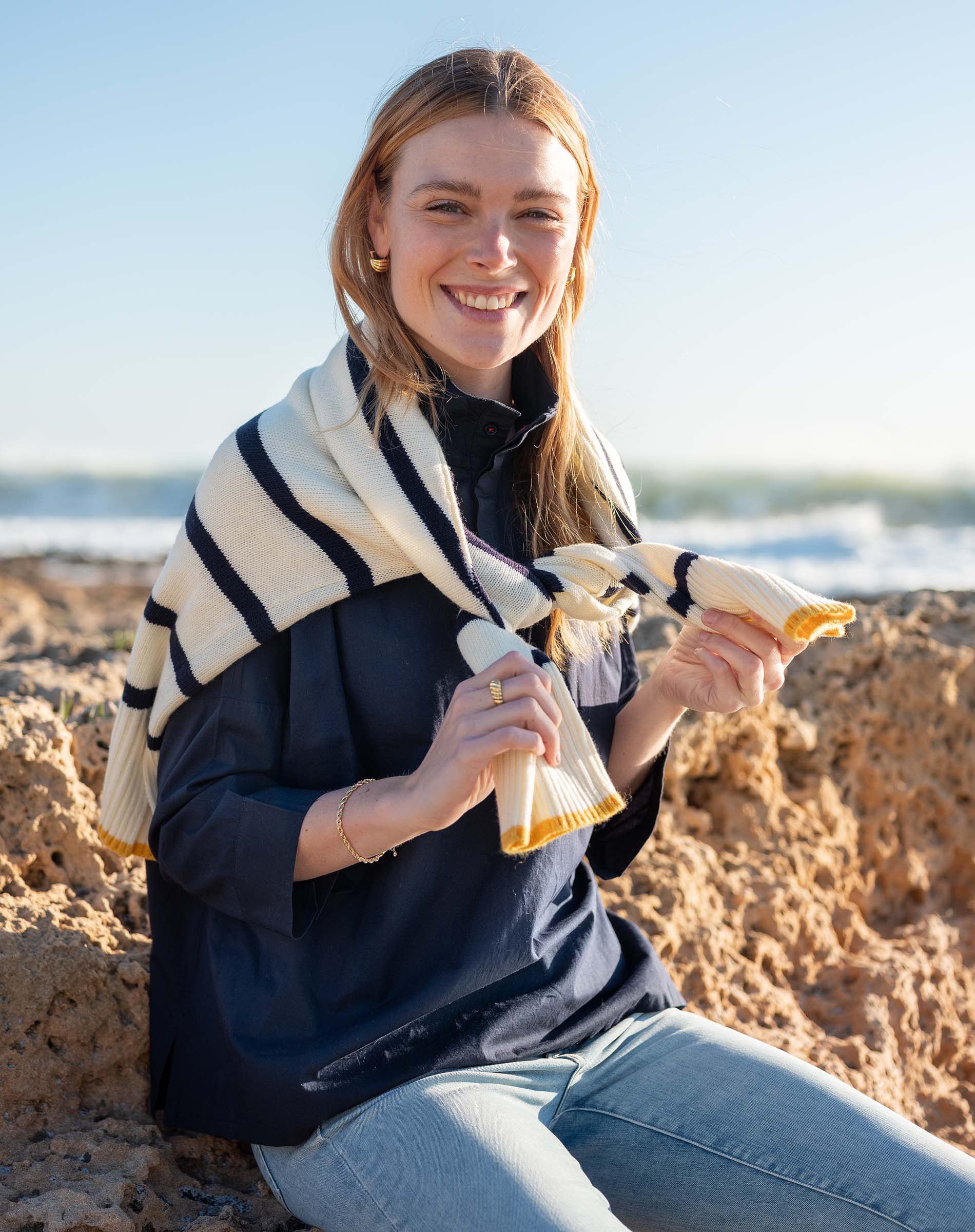 Woman sitting on a beach holding a striped towel