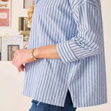 Person wearing a blue and white striped shirt with rolled-up sleeves, standing against a neutral background.
