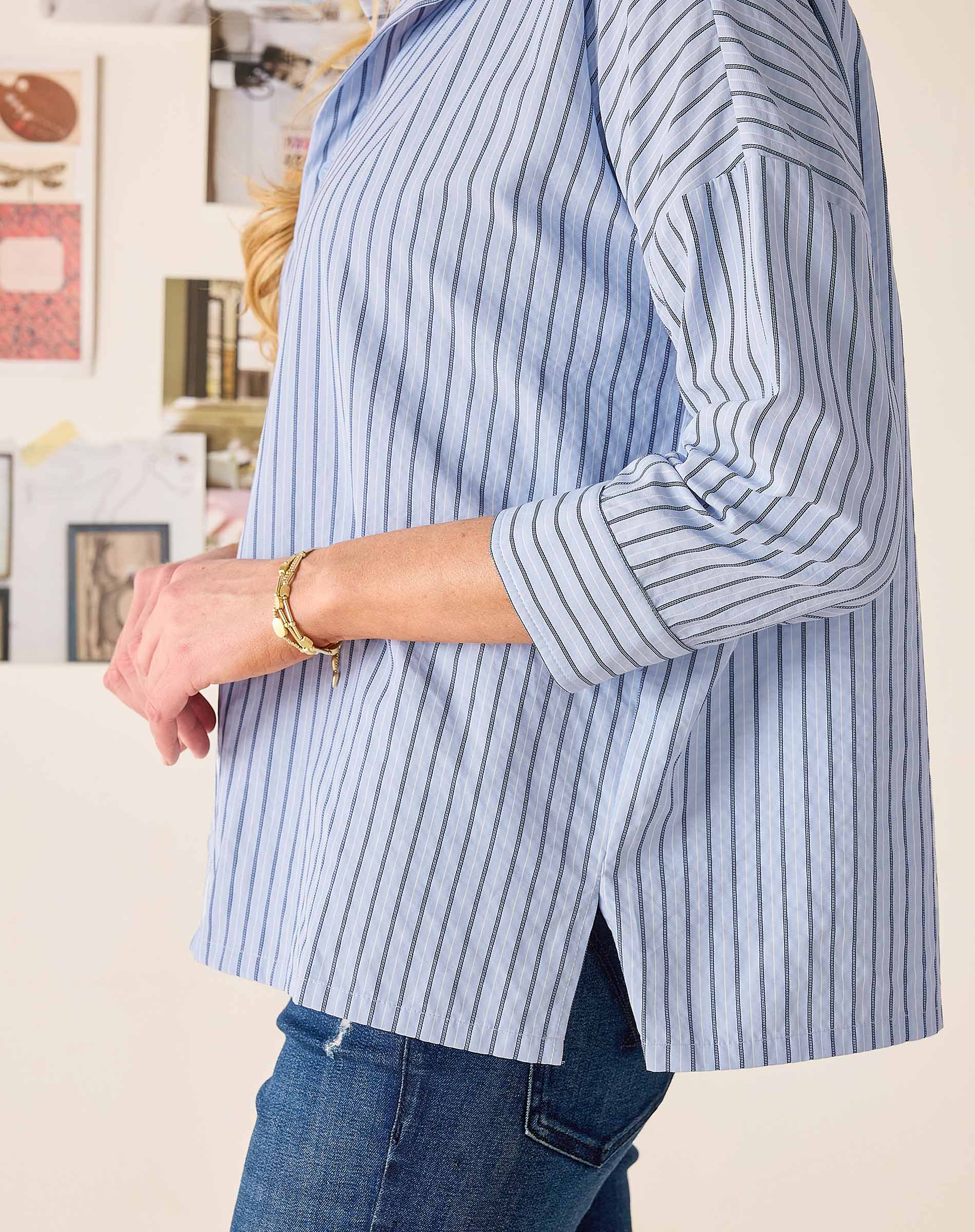 Person wearing a blue and white striped shirt with rolled-up sleeves, standing against a neutral background.
