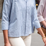 Person wearing a blue and white striped shirt with beige pants, standing outdoors.