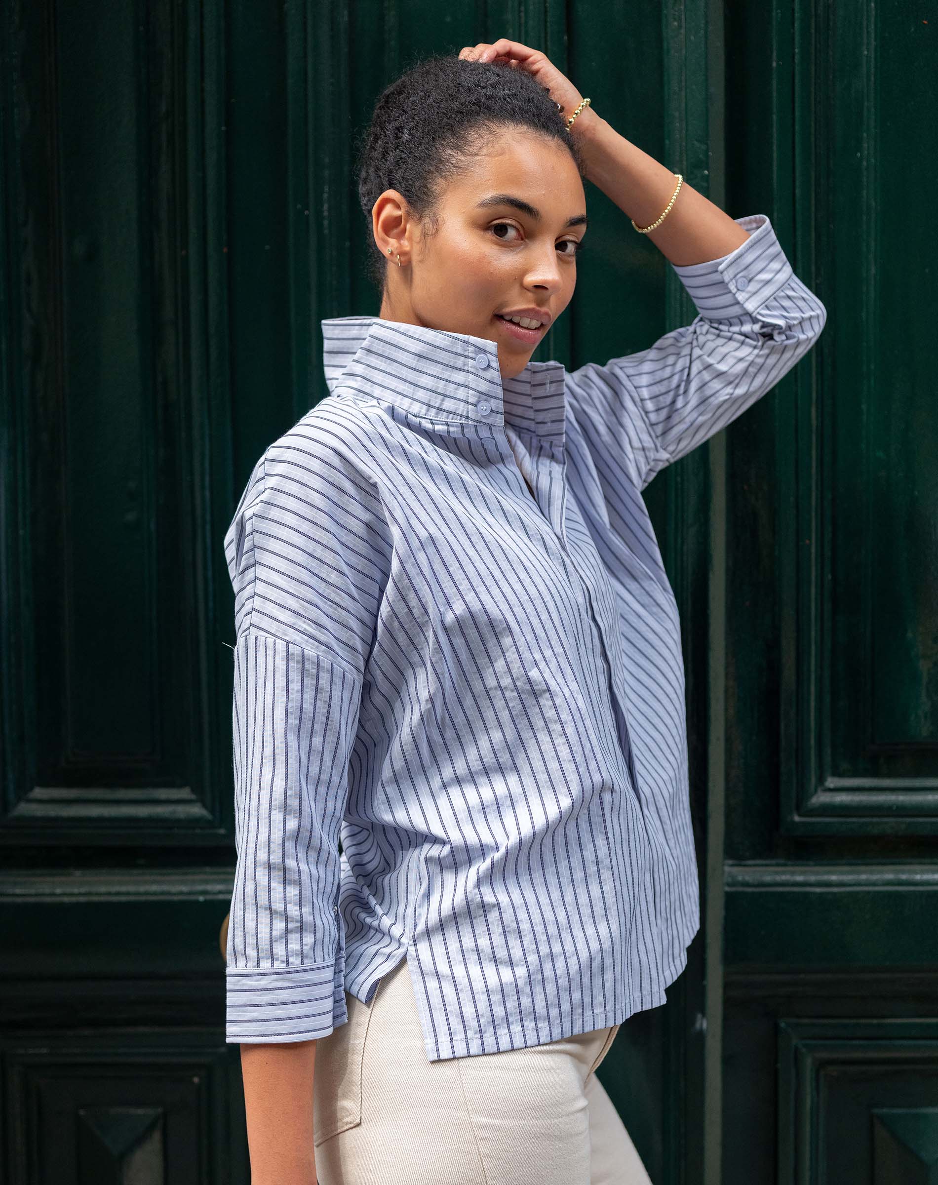 Woman wearing a blue and white striped shirt against a dark green door.