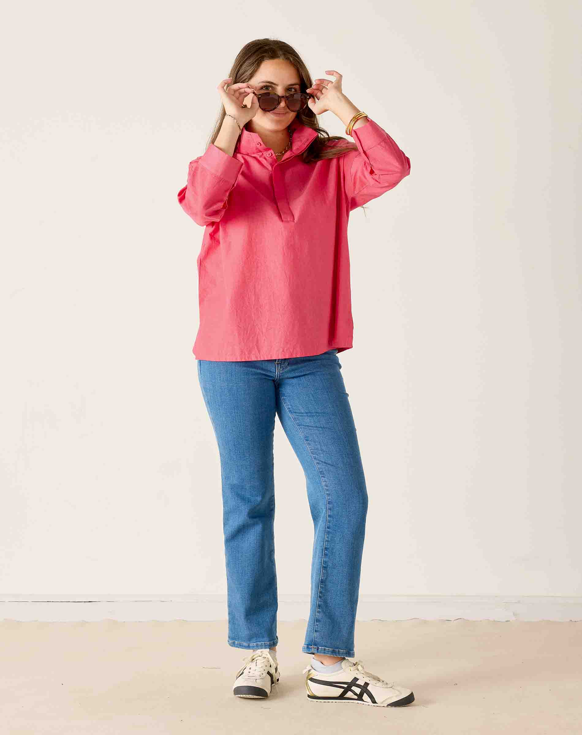 Woman wearing a pink jacket and blue jeans against a white background