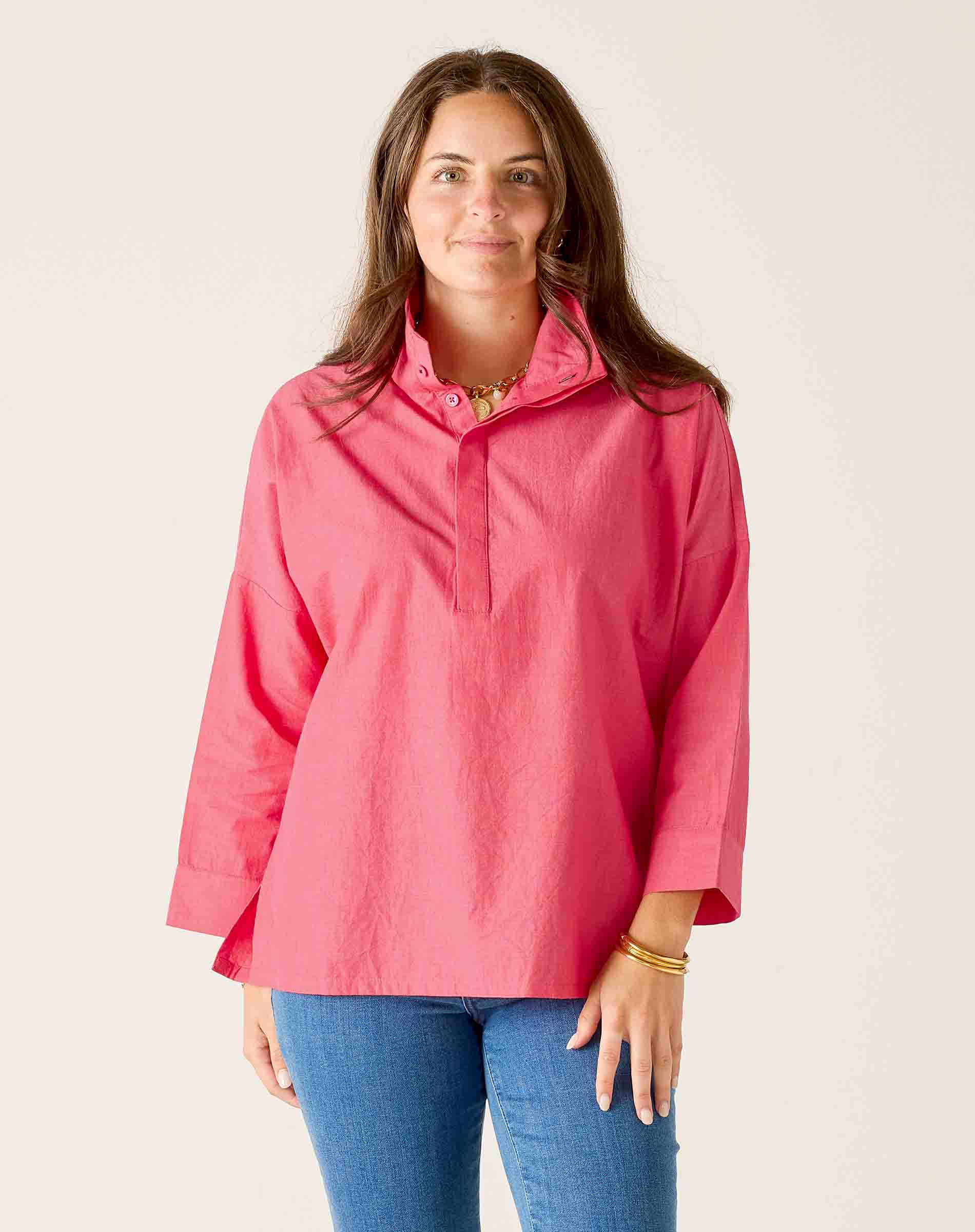 Woman wearing a pink long-sleeve shirt and blue jeans against a white background