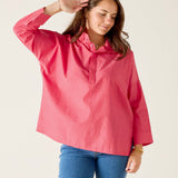 Woman wearing a pink shirt and blue jeans against a plain background