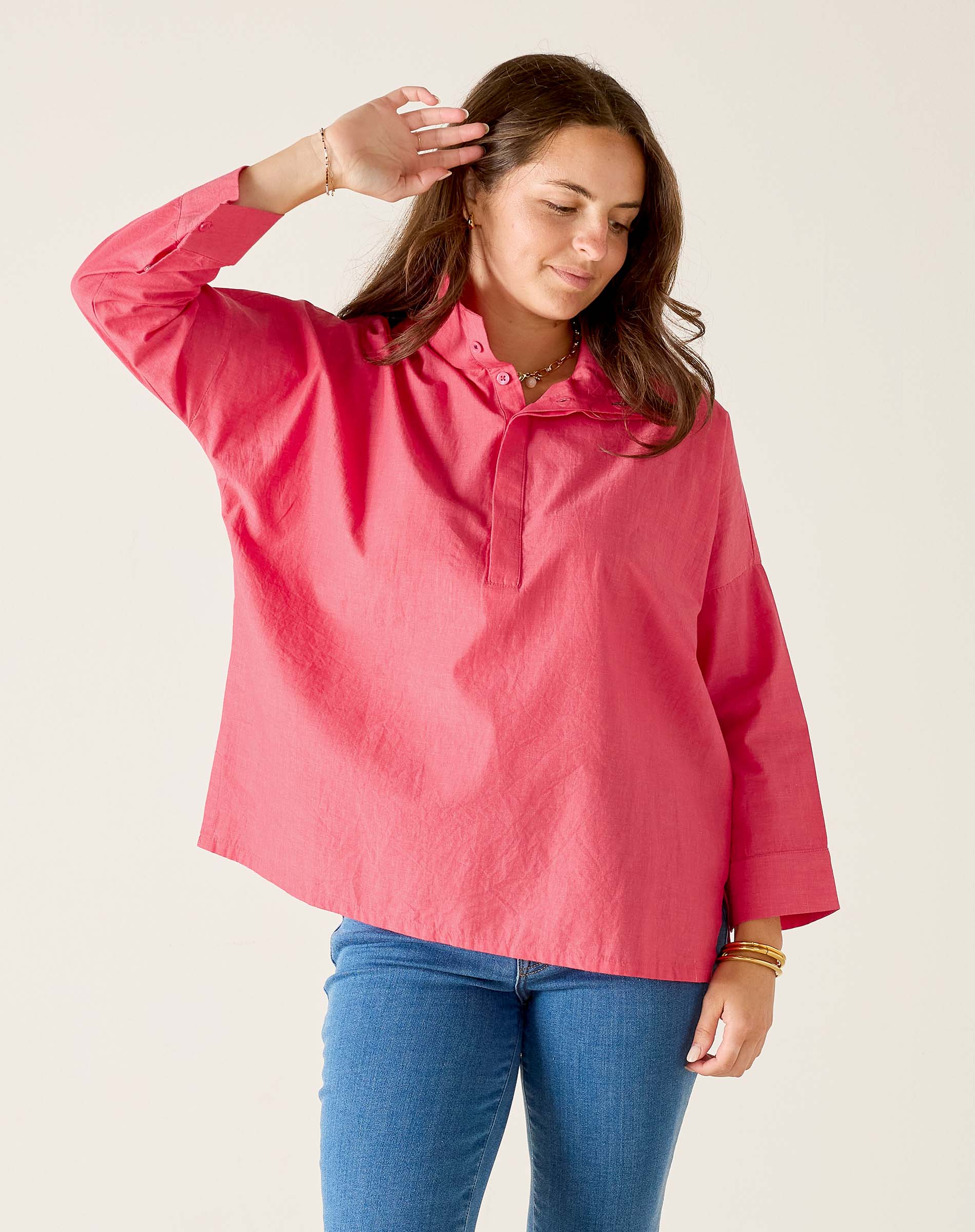 Woman wearing a pink shirt and blue jeans against a plain background