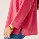 Person wearing a pink shirt and blue jeans with gold bracelets on a plain background
