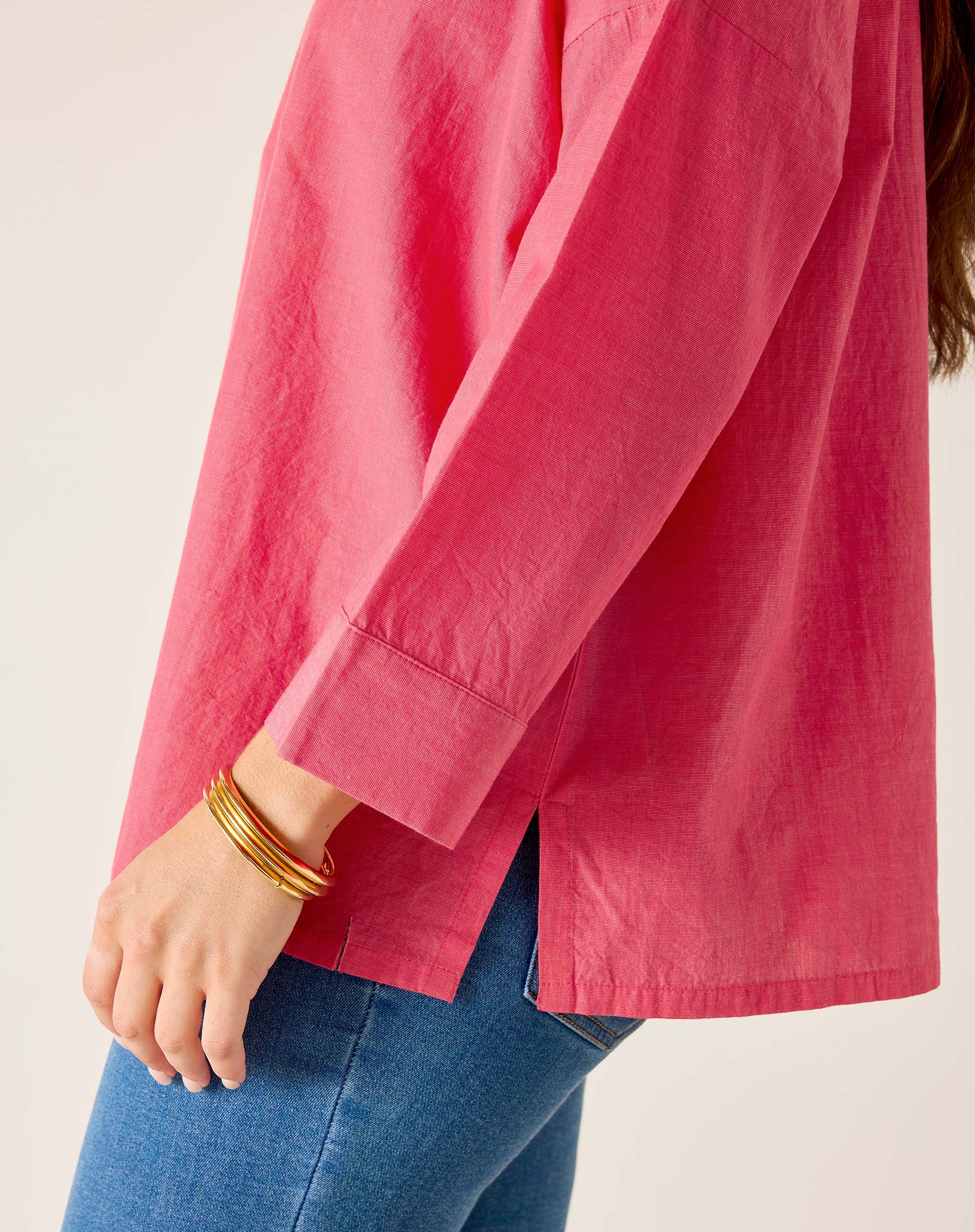 Person wearing a pink shirt and blue jeans with gold bracelets on a plain background