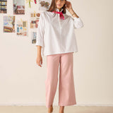 Woman wearing a white blouse and pink pants against a light background