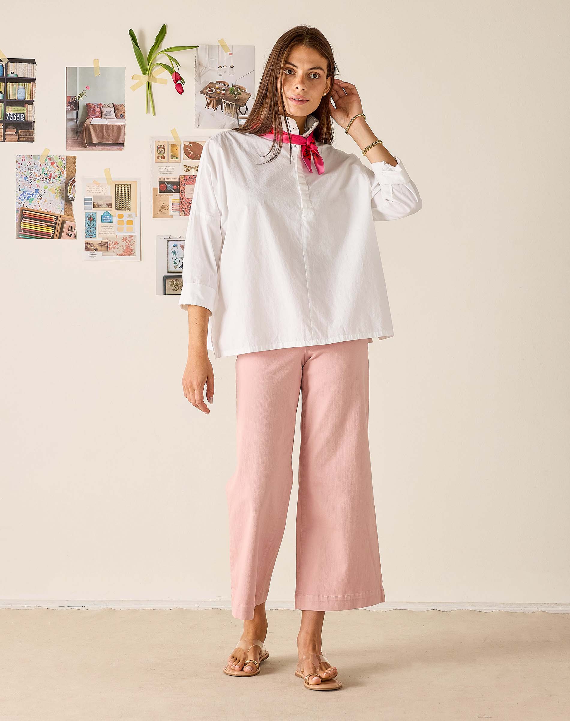 Woman wearing a white blouse and pink pants against a light background
