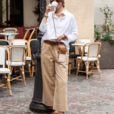 Woman in white shirt and beige pants standing on a street with cafe chairs in the background