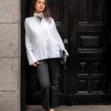 MERSEA ladies' travel-ready white tuxedo style tunic top with intricate embroidery and a high neck, paired with dark grey trousers.