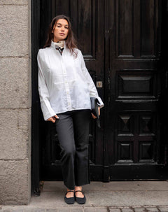 MERSEA ladies' travel-ready white tuxedo style tunic top with intricate embroidery and a high neck, paired with dark grey trousers.
