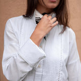 White cotton tuxedo top with pleated front panels and embroidered detailing.