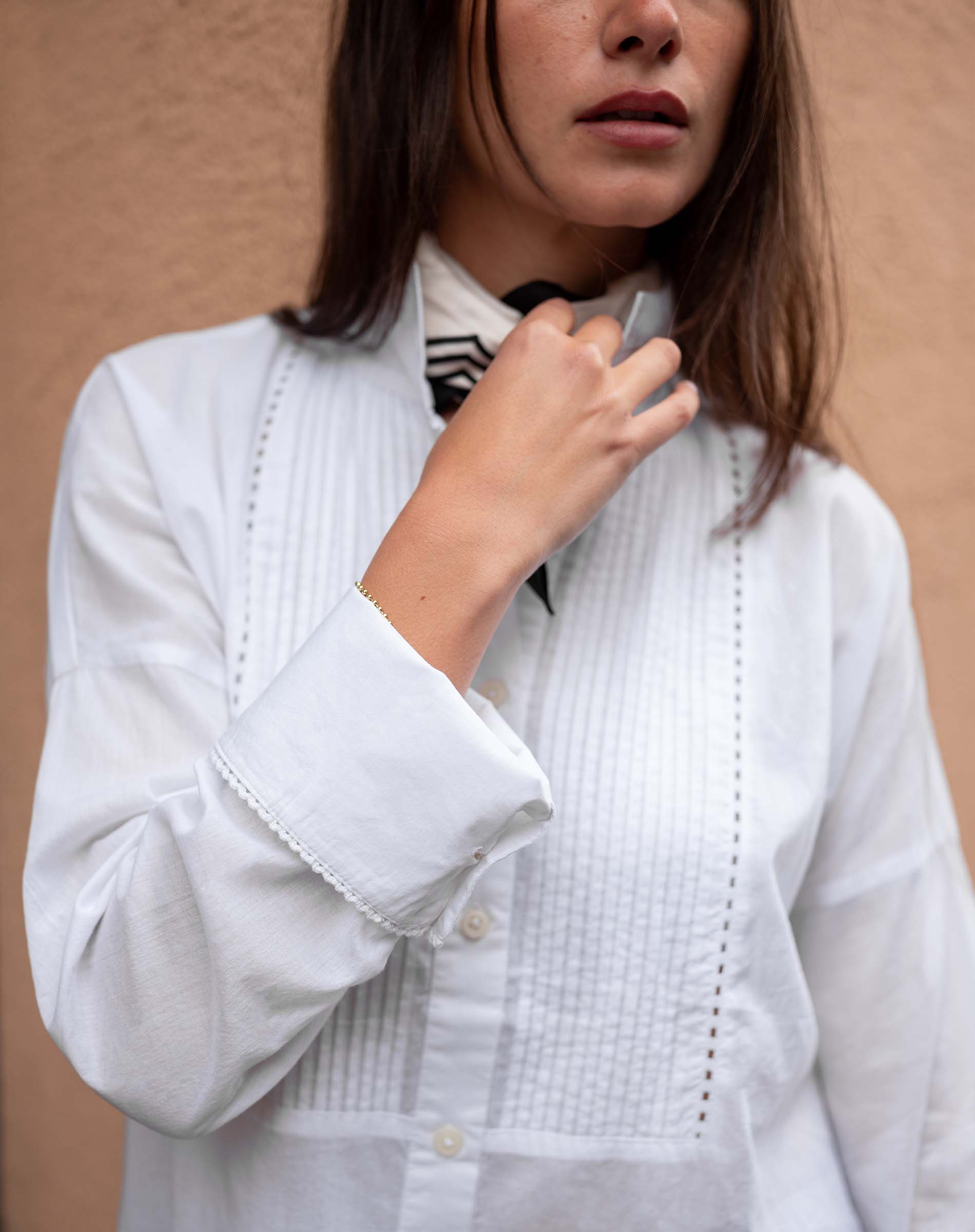 White cotton tuxedo top with pleated front panels and embroidered detailing.
