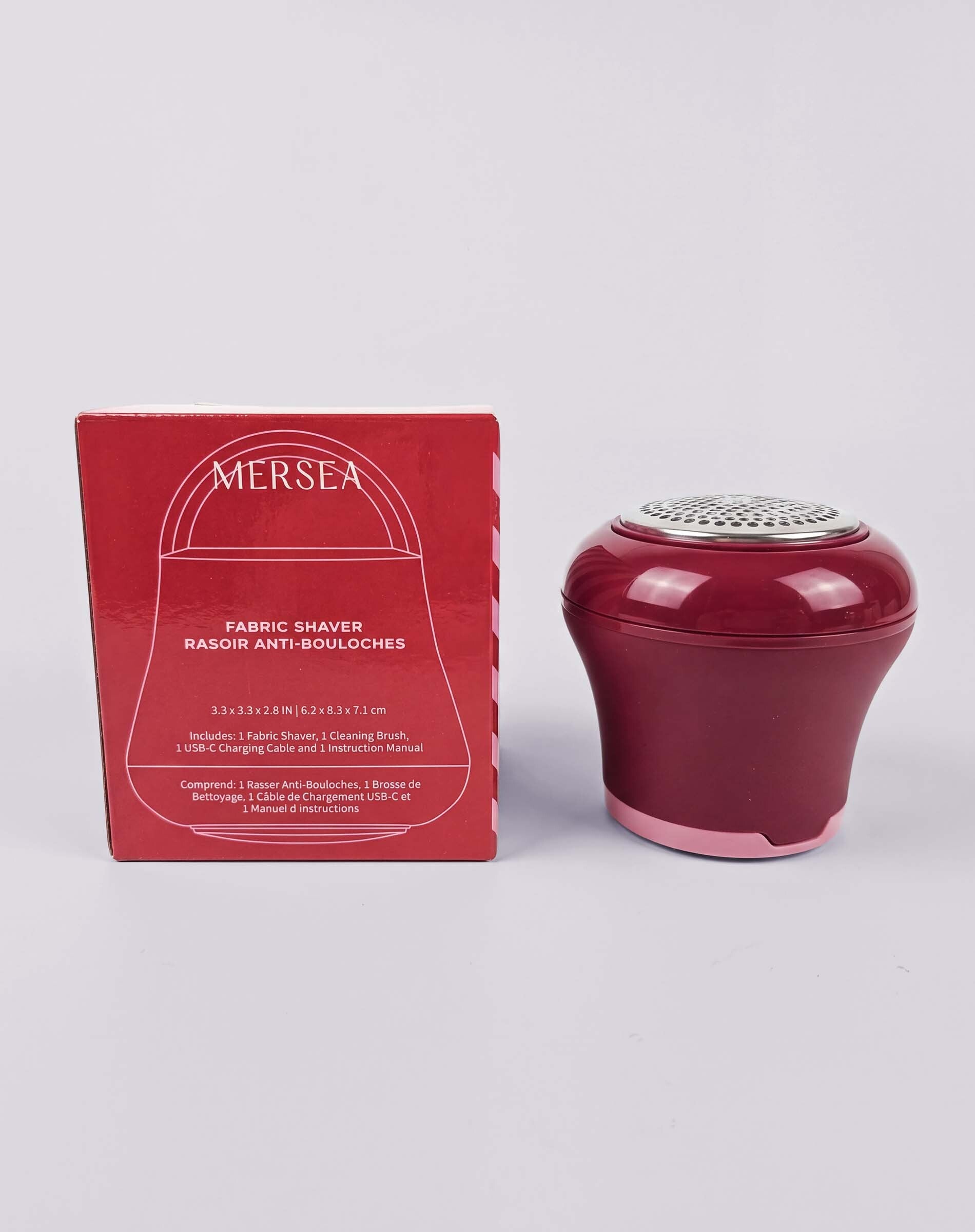 Ruby red portable fabric shaver and matching box. Text: MERSEA, FABRIC SHAVER, RASOIR ANTI-BOULOCHES, 33x35x20_mmx20x33x31_cm, Inscrit: Fabric Shaver | French: Rasoir Anti-Bouloches, LISE Clothing Group | Français: MERSEA, Conforme à la directive 2011/65/UE, Consignes de sécurité, Manuel d'instructions.