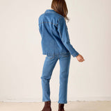 Back view of the medium blue denim jacket and matching jeans with a model in brown boots.