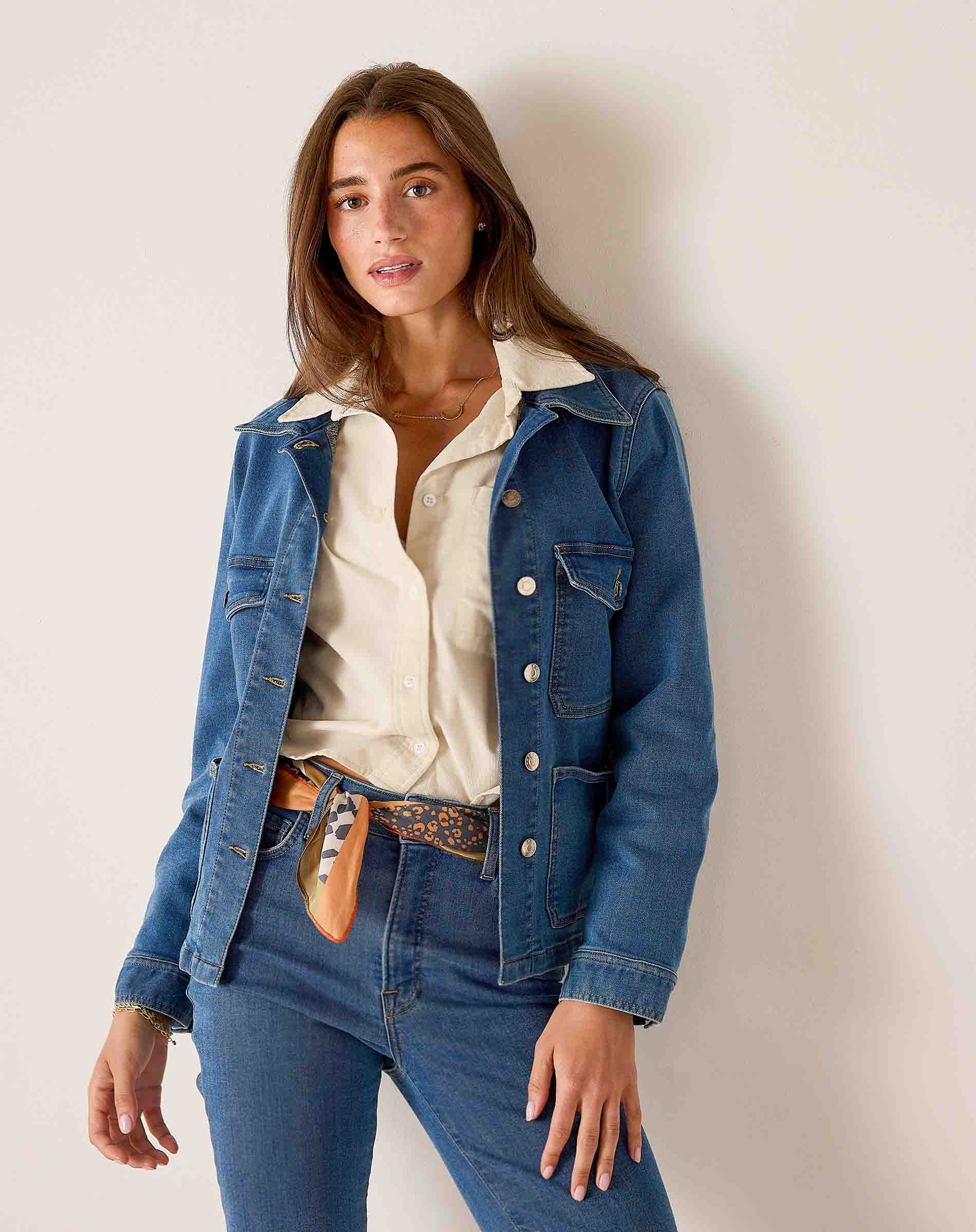 Blue denim field jacket with buttons over a cream button-down shirt and jeans.