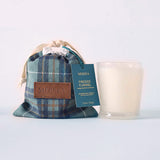 MERSEA women's travel-friendly fireside flannel plaid candle gift set featuring a blue and green plaid bag with a card that reads 'MERSEA FIRESIDE FLANNEL' and an accompanying white candle in a clear glass jar. Text: MERSEA, FIRESIDE FLANNEL, longer nights, cozy vibes, scented for 2 candles. 7.5 oz / 206 g.