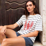 Woman wearing a striped shirt with a red graphic sitting against a textured wall.