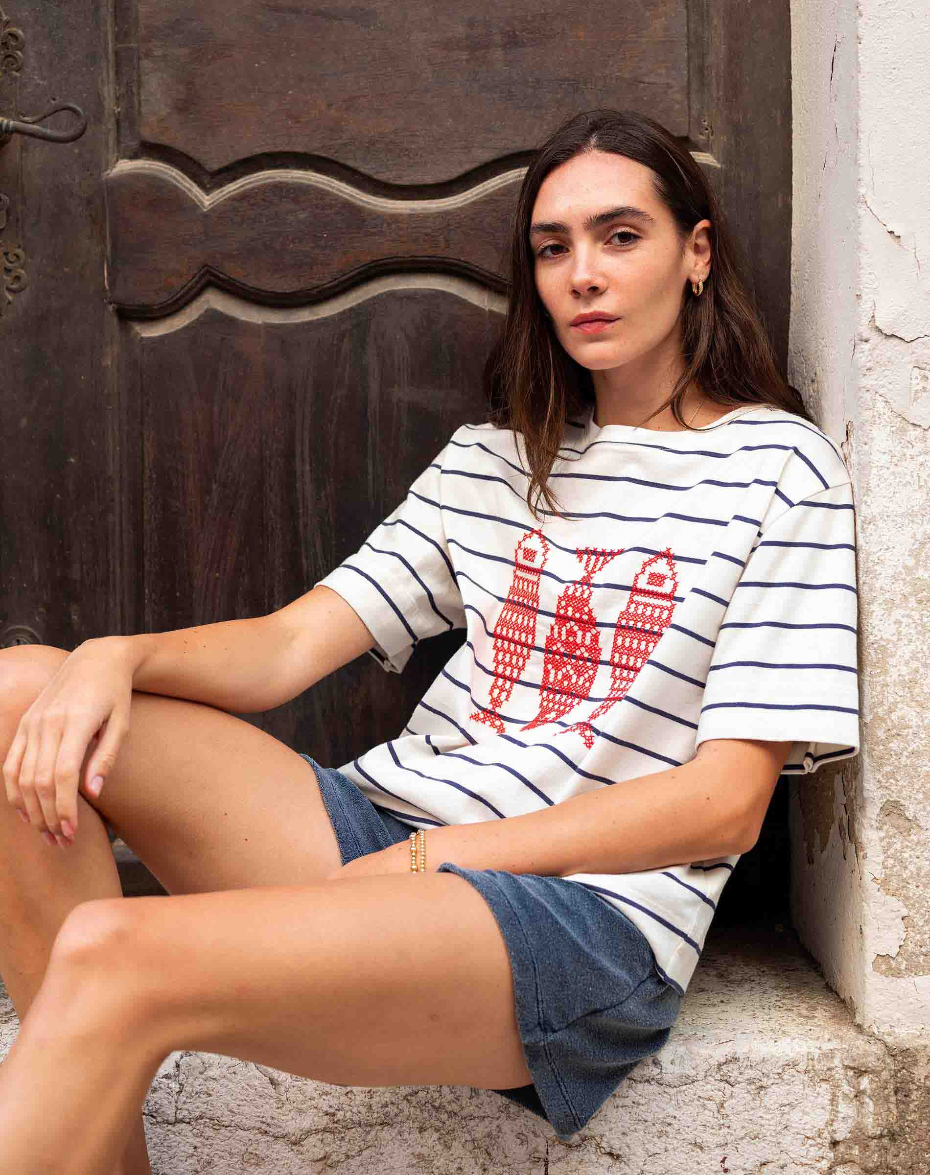 Woman wearing a striped shirt with a red graphic sitting against a textured wall.