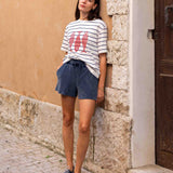 Woman wearing a striped shirt and shorts standing against a stone wall.