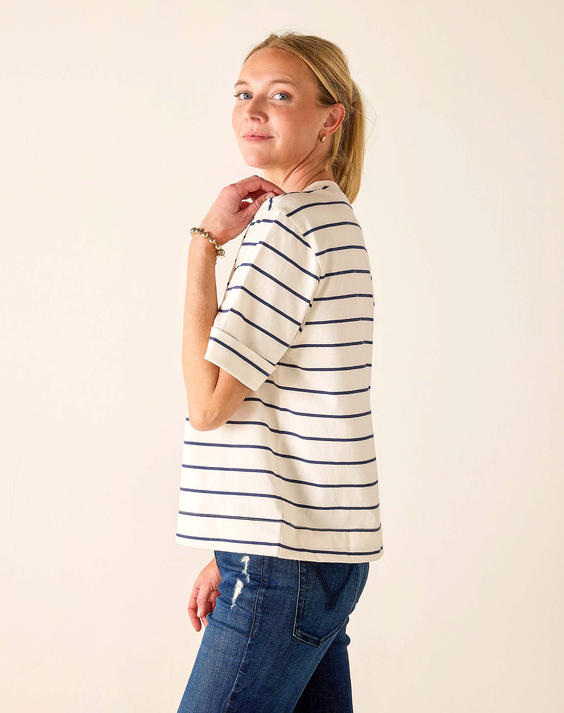 Woman wearing a striped shirt and jeans against a plain background