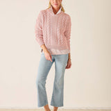 Woman wearing a pink cable knit sweater and light blue jeans on a plain background
