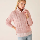 Woman wearing a pink cable knit sweater against a plain background