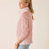 Woman wearing a pink cable knit sweater against a plain background