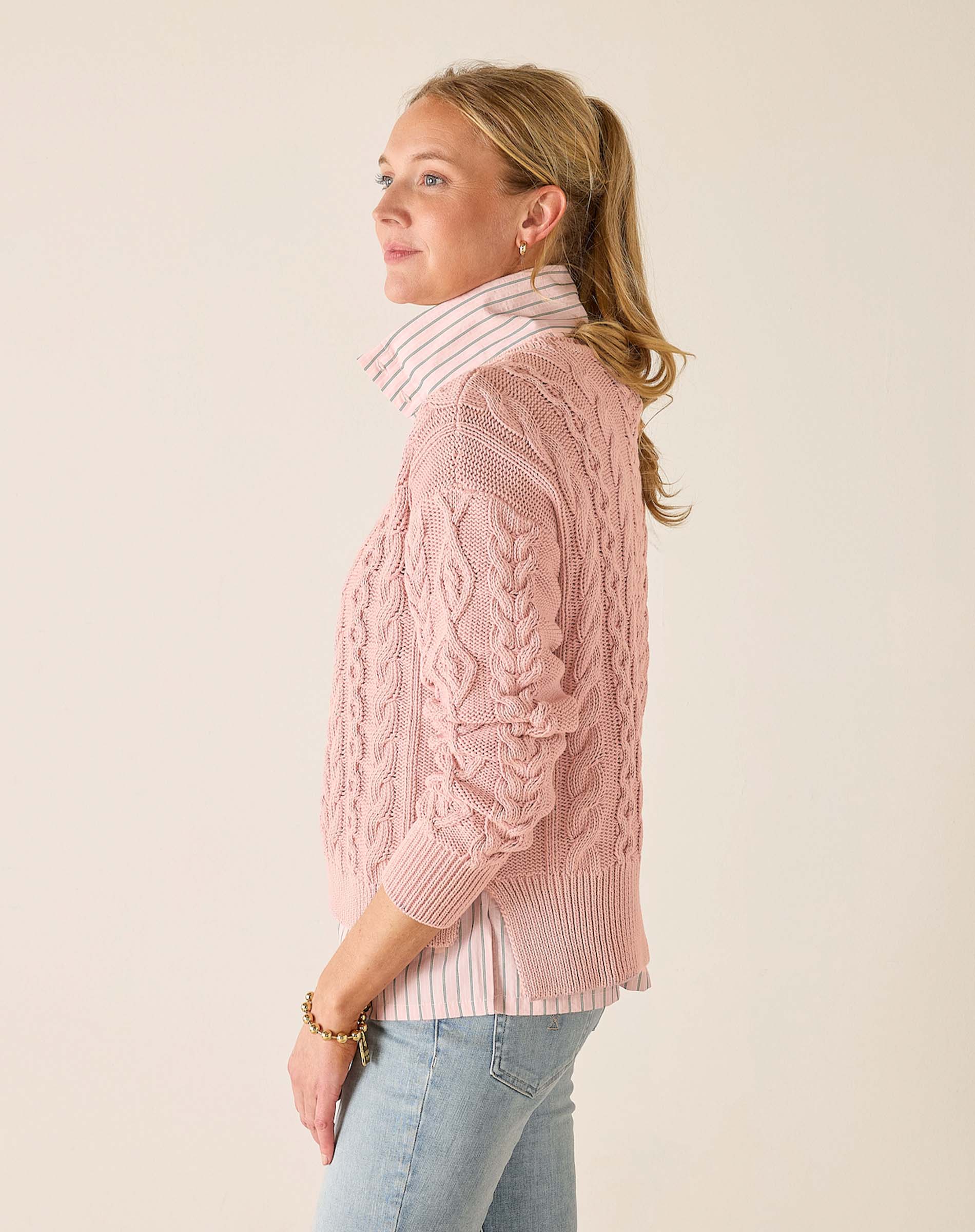 Woman wearing a pink cable knit sweater against a plain background