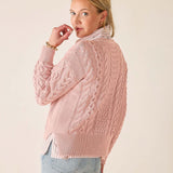 Woman wearing a pink cable knit sweater against a plain background