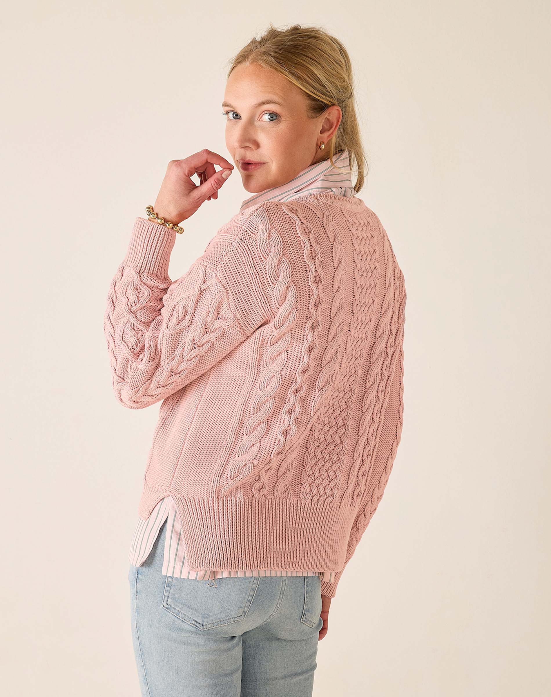 Woman wearing a pink cable knit sweater against a plain background